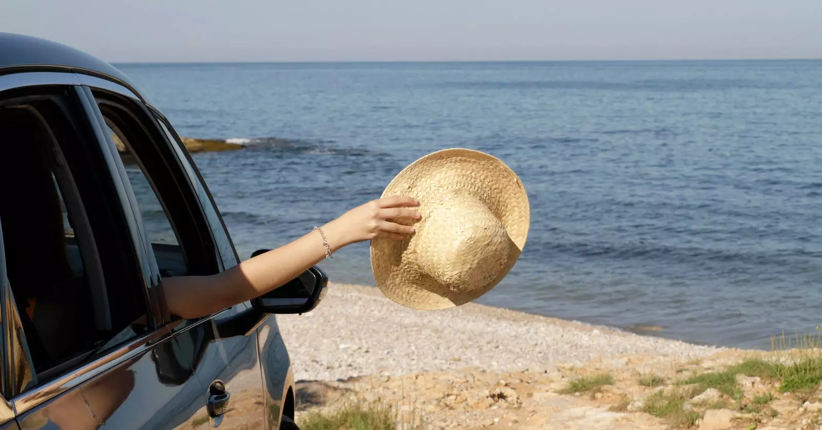 Wanita menjulurkan topi keluar dari tingkap kereta di pantai