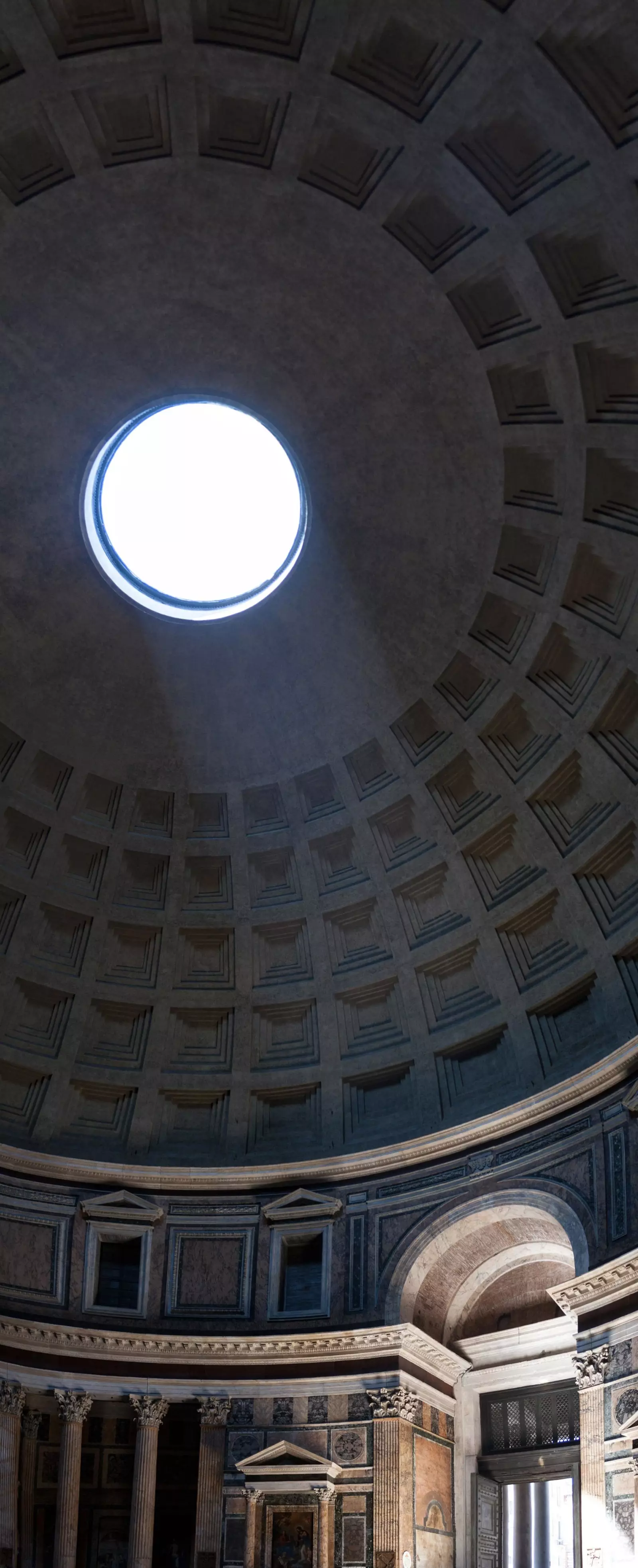 La llum que ingressa per l'òcul il·lumina la porta d'entrada al Panteó