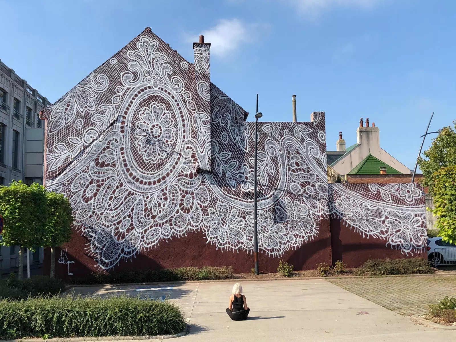 O artista NeSpoon em frente ao mural de renda que cobre uma antiga fábrica têxtil em Calais, França.