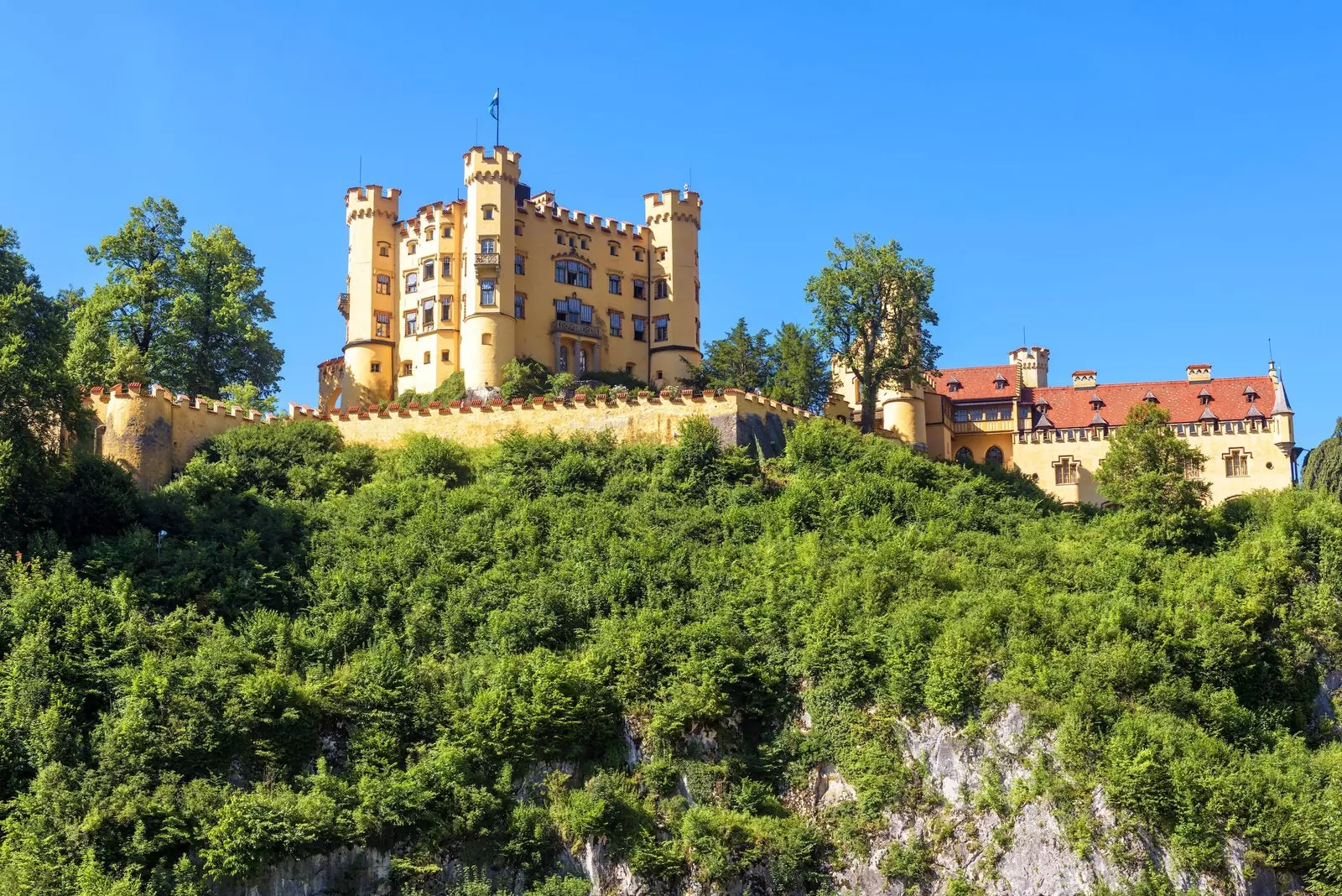 O imponente e defensivo amarelo Hohenschwangau Palace no topo de uma montanha na Baviera.