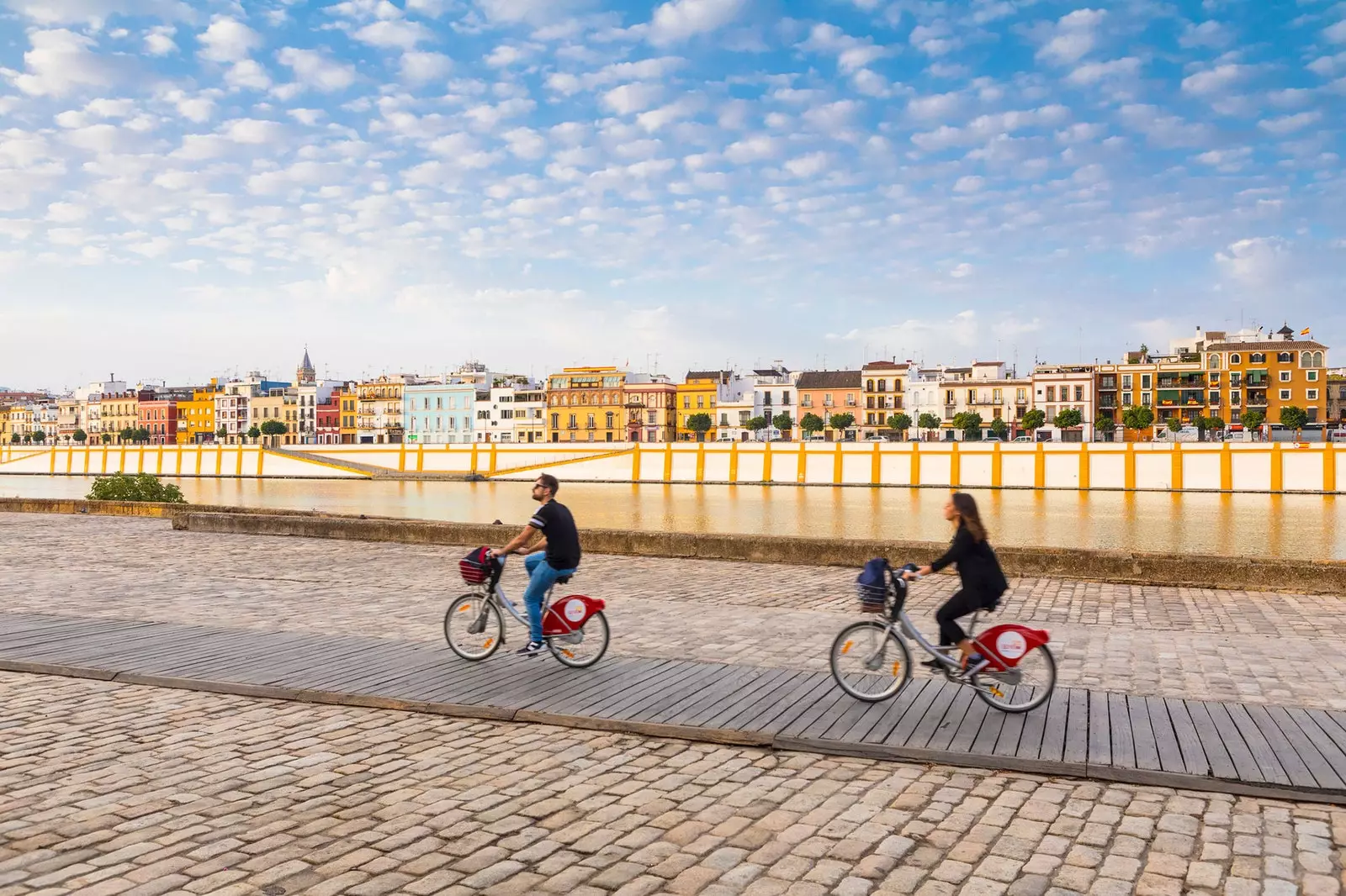 Two people riding a bicycle in front of the Triana neighborhood in Seville