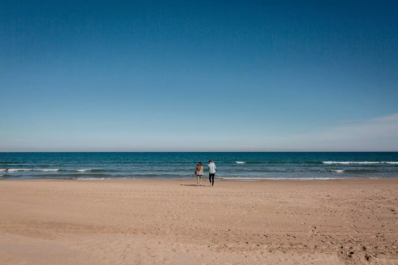 Uma família caminha por uma praia vazia em Gandía