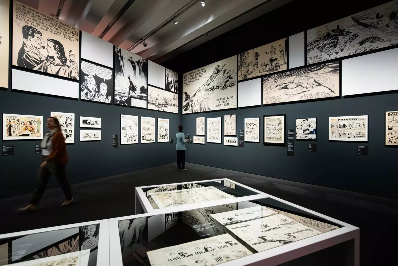 Orang-orang berjalan melalui pameran 'Cómic. Dreams and history' dan amati ilustrasi yang dipamerkan.