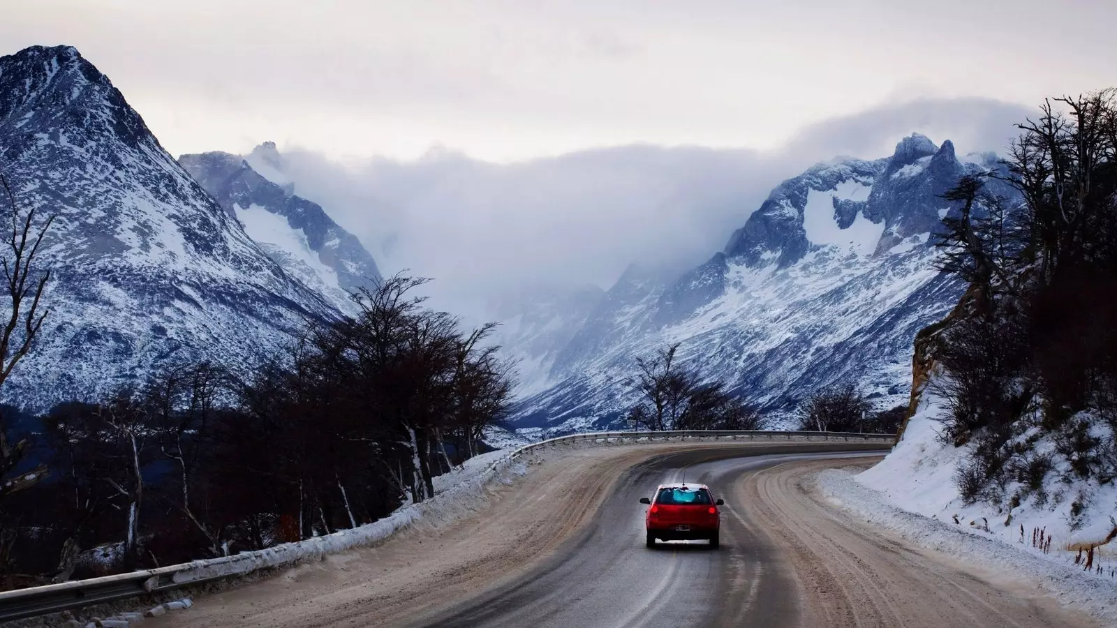 Punainen auto ajaa aution moottoritien läpi Patagonian lumisissa maisemissa.