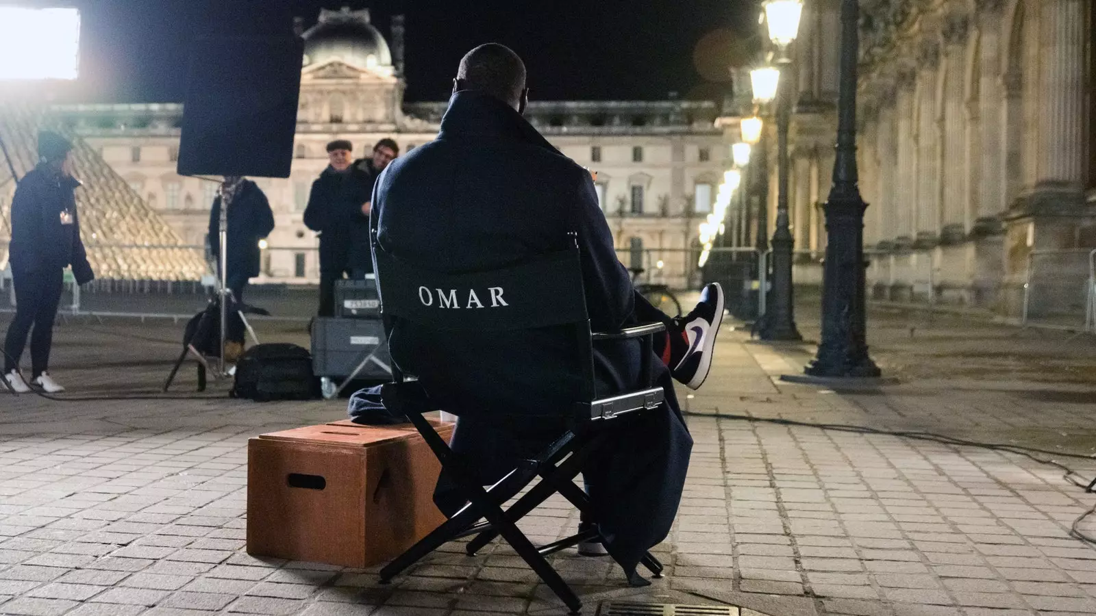 Omar Sy durante as filmagens em frente ao Louvre e a pirâmide de vidro de Ieoh Ming Pei.