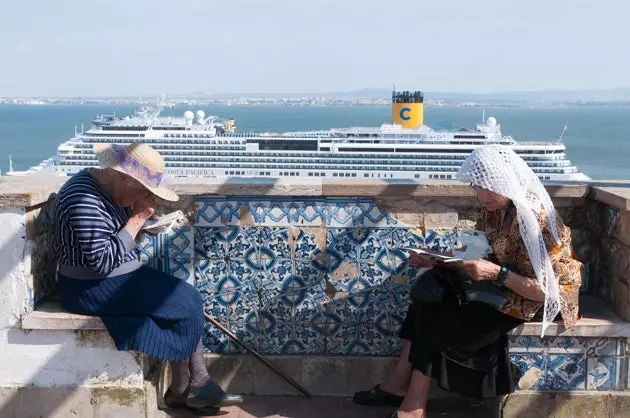 Duas mulheres aproveitam o sol e as vistas dos navios de cruzeiro no Miradoiro de Santa Luzia.