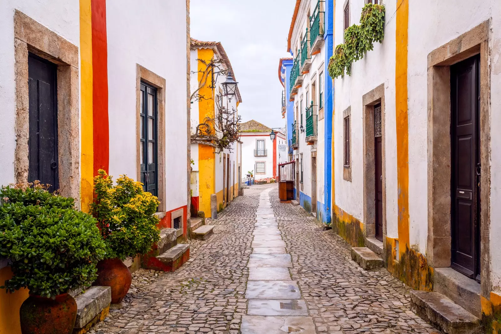 Rua de paralelepípedos e casas brancas com varandas cheias de plantas e decorações em cores vivas em Óbidos.