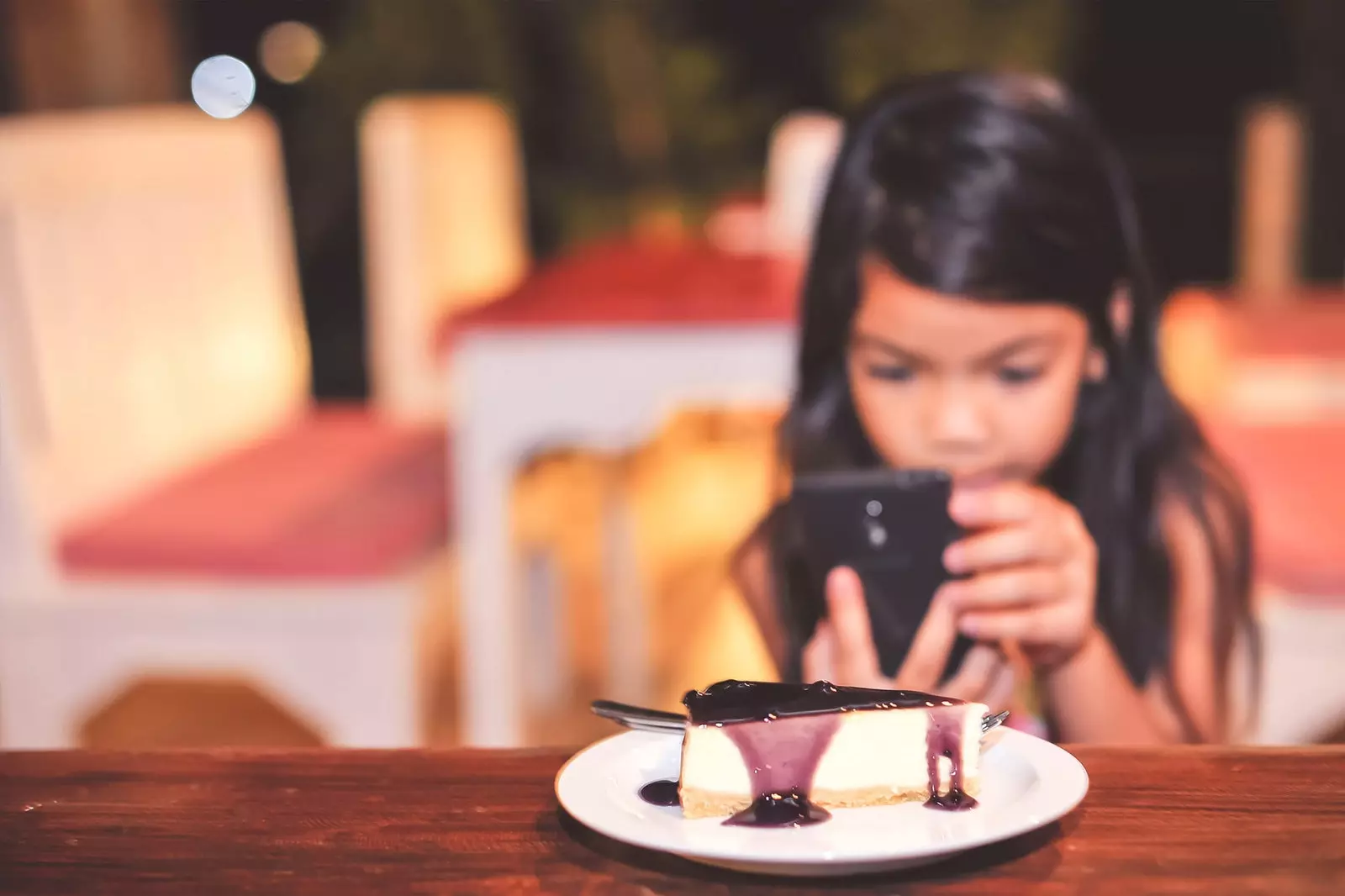 gadis dengan ponsel di depan kue