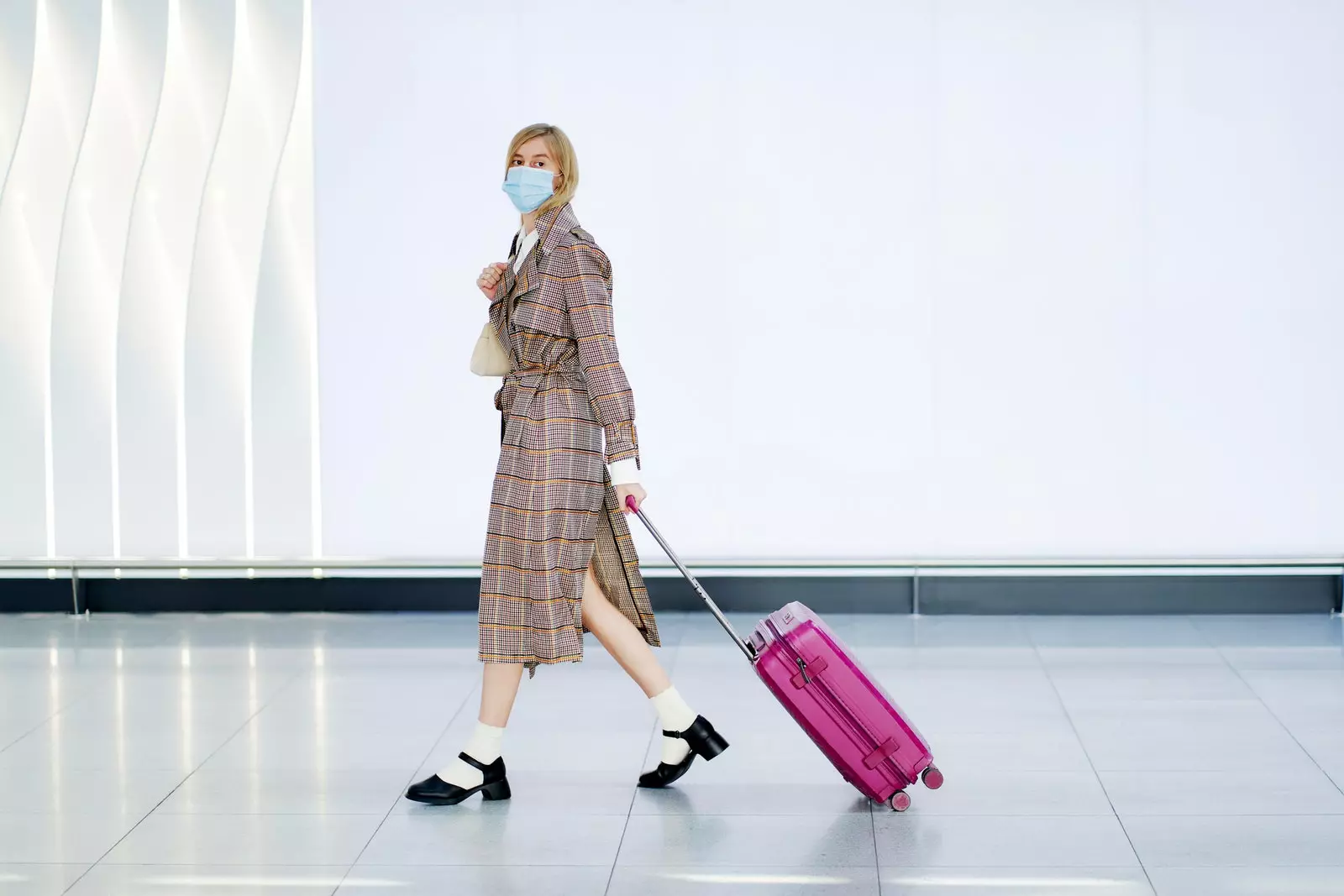 Woman in airport with mask carrying a suitcase