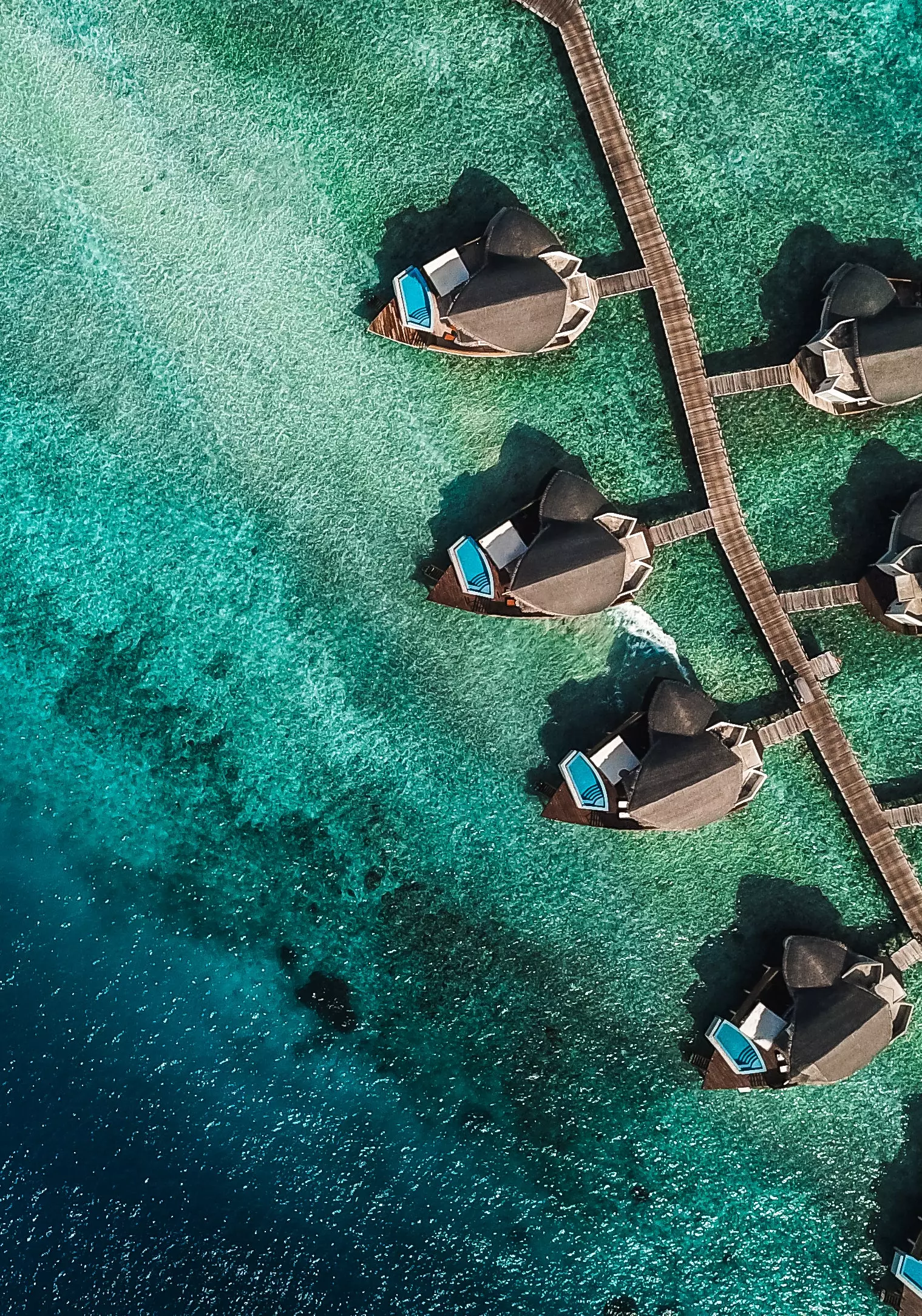 Luftaufnahme mehrerer Häuser mit Swimmingpool über türkisfarbenem Wasser auf den Malediven