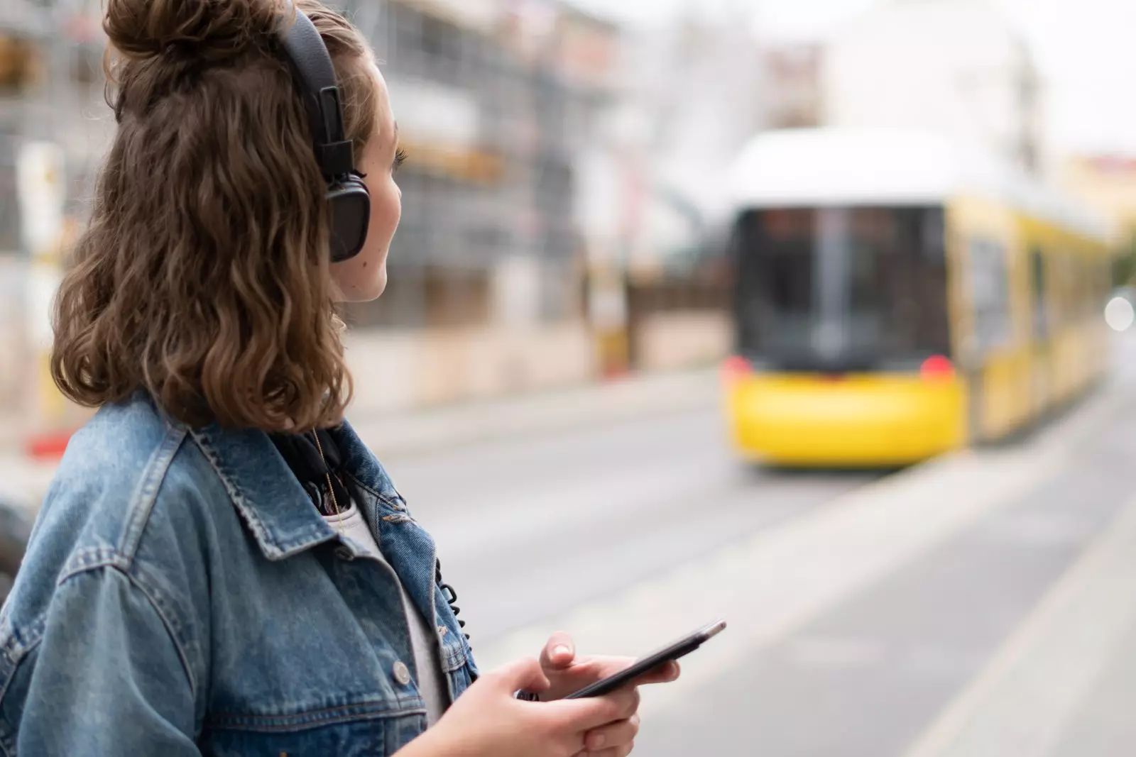 fată cu căști și telefon mobil care așteaptă tramvaiul