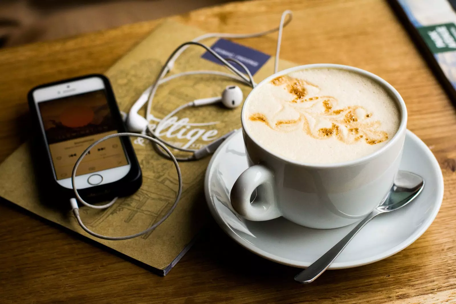 Mobiles Café mit kleinen Kopfhörern und Notizbuch auf Holztisch.