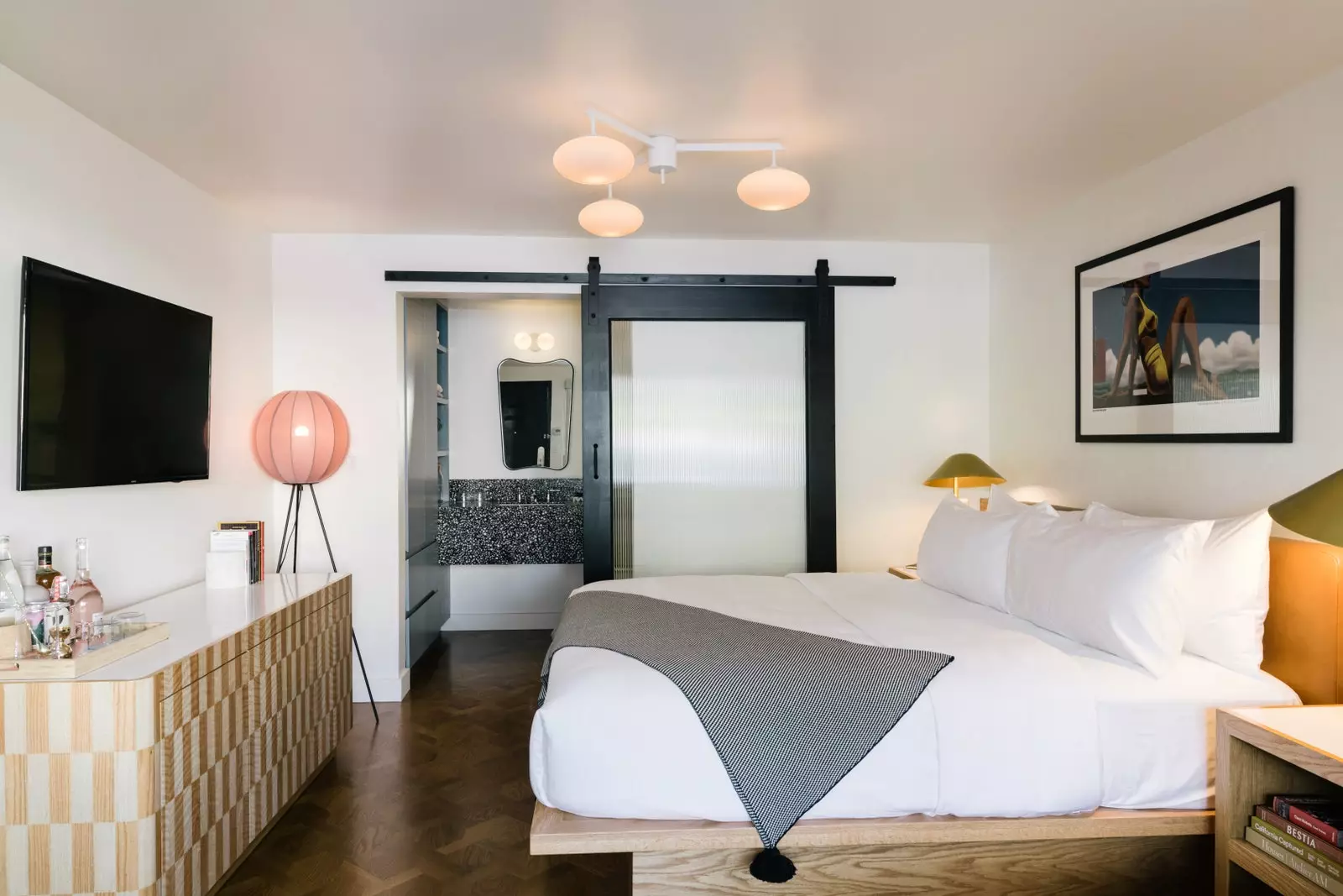 Bedroom with double bed and white sheets pink lamps and TV on the wall