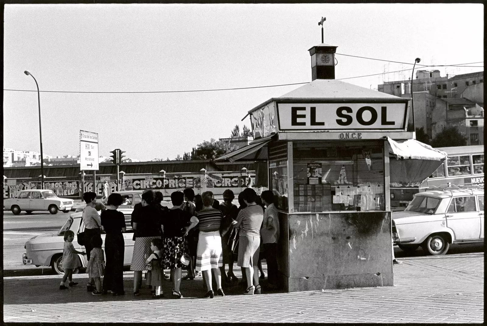 Picha nyeusi na nyeupe ya kikundi cha wanawake cha Javier Campano wakikimbilia kwenye kivuli cha kioski huko Madrid 1977.