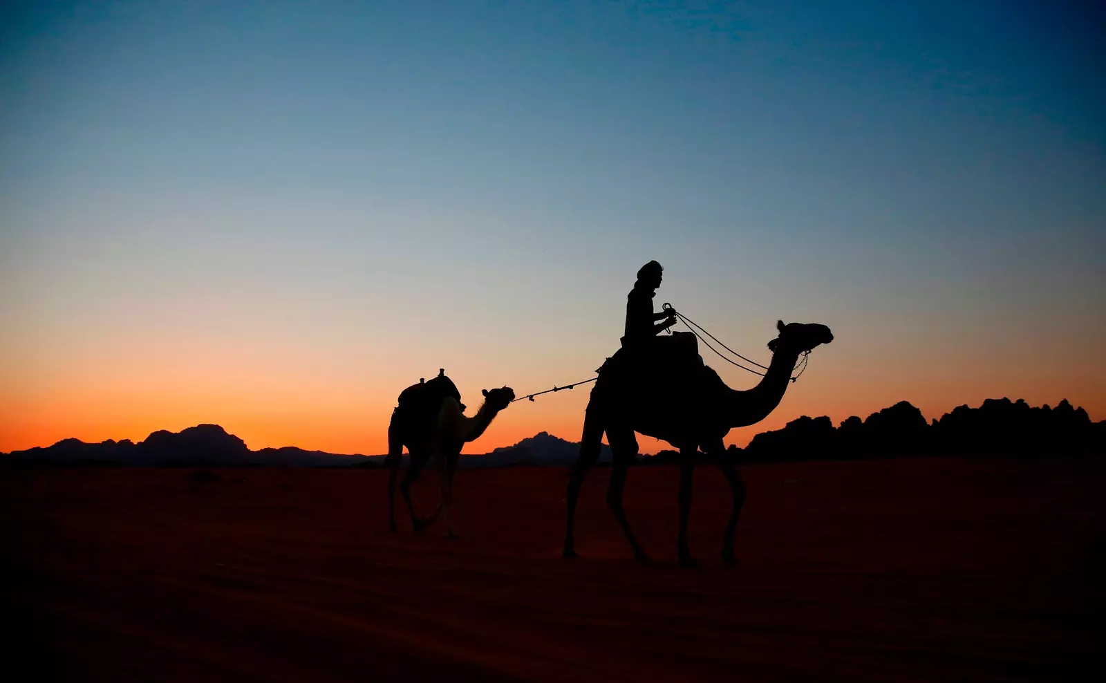 Egy tevén lovagló személy sziluettje naplementekor a Wadi Rum sivatagban, Jordániában