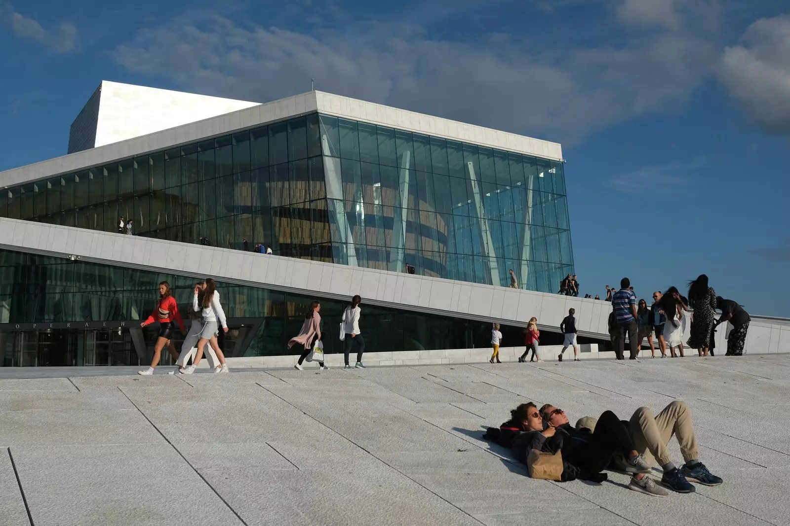 Several people lying and walking in the upper walkable area of ​​the Oslo Opera House