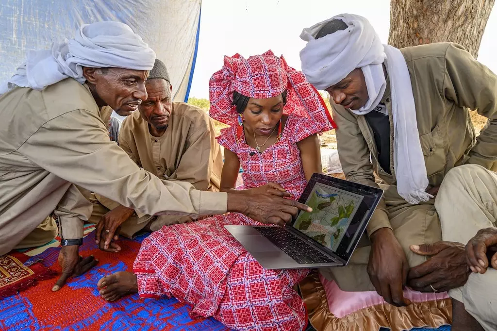 Den Hindou Oumarou Ibrahim ëmgi vun dräi Leit an hält e Laptop