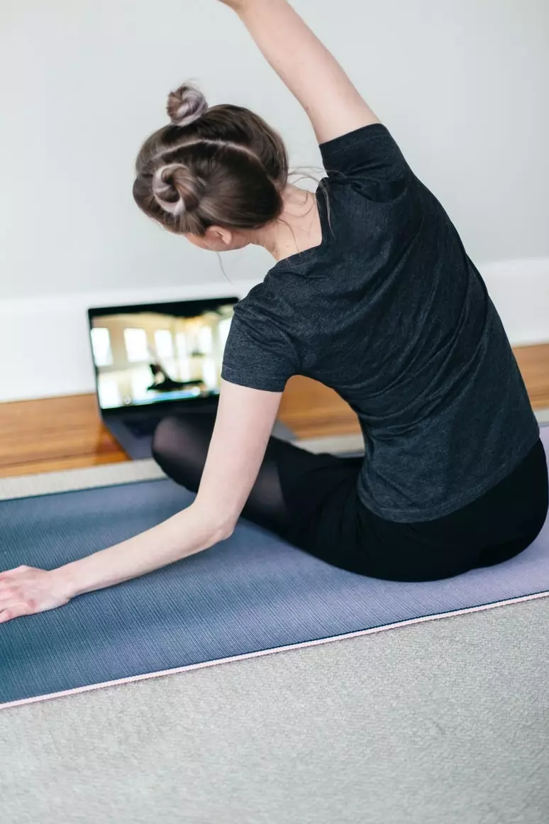 Person på rygg på en matta som kopierar en yogaställning från en bärbar dator