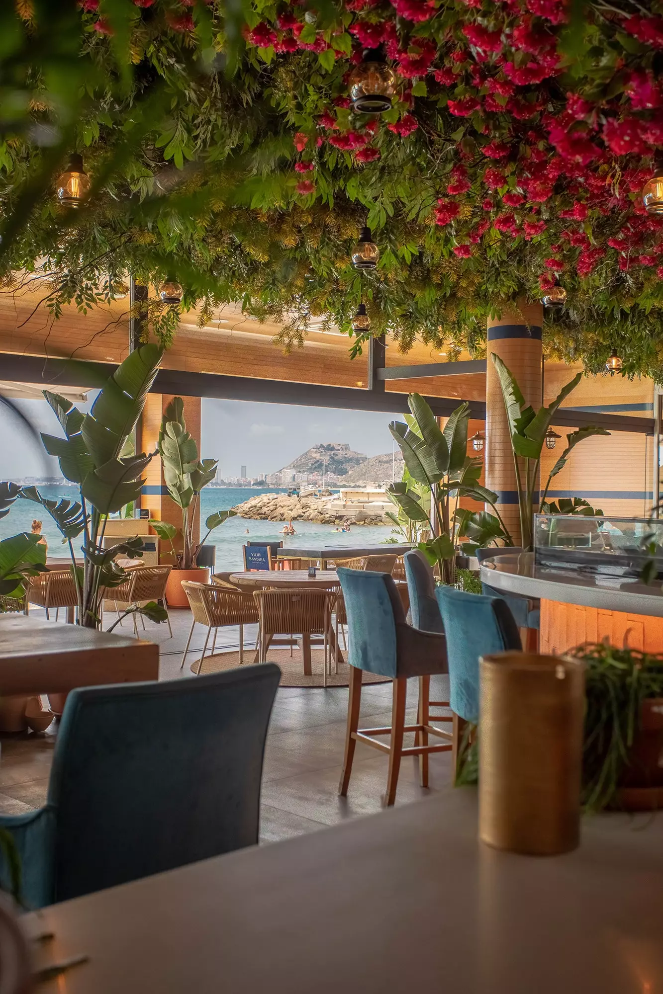 O interior da Villa Bandida com decoração vegetal de cores claras de madeira e aberto para a praia.