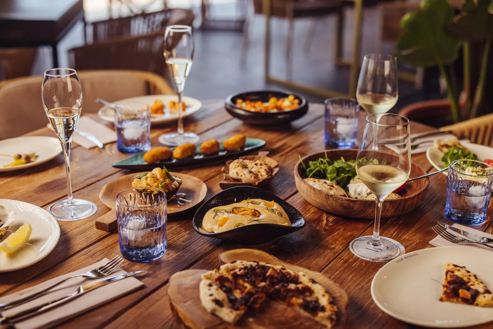 Borð á Villa Bandida með pizzum, krókettum, salötum, hvítvínsglösum og vatni.