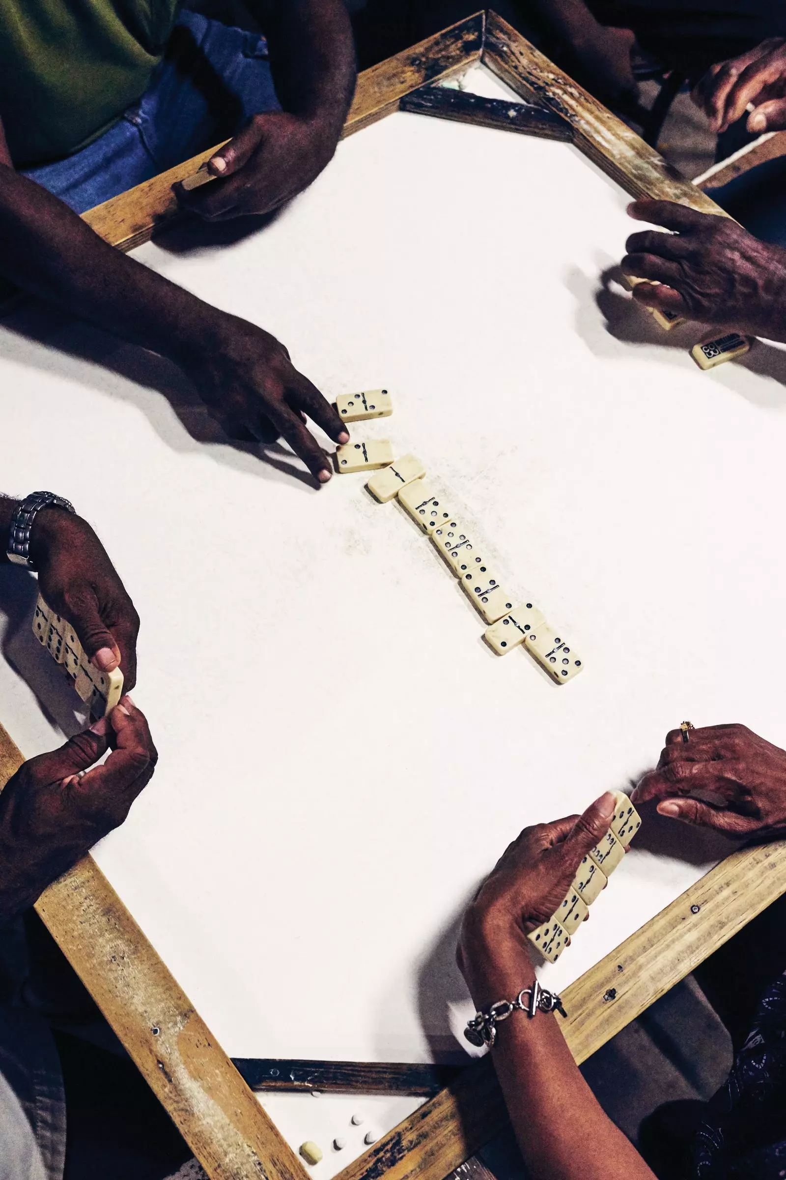 Domino table from above with four pairs of hands playing