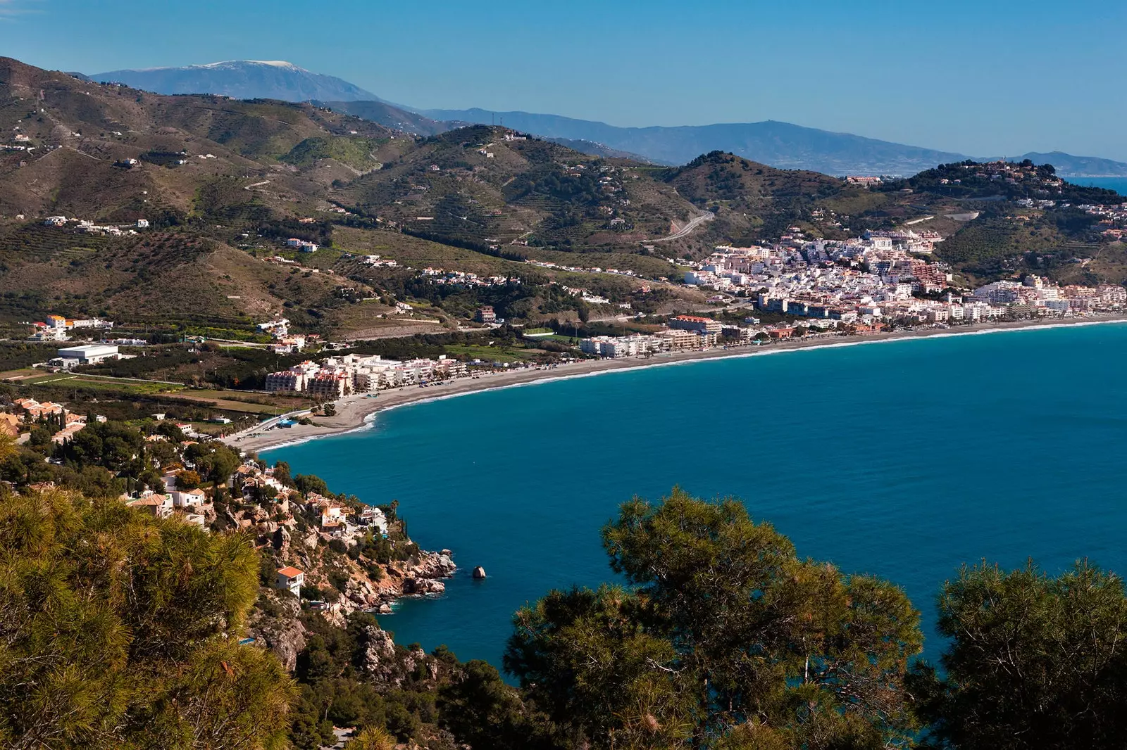 Luftfoto af den 2 kilometer lange middelhavsstrand La Herradura mellem to klippefremspring, der skaber formen...