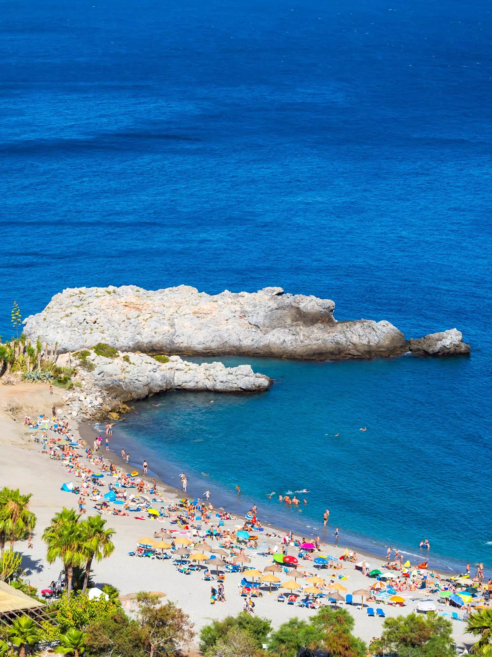 La spiaggia di La Herradura con la sabbia piena di vacanzieri tra gli affioramenti rocciosi che si gettano nel mare.