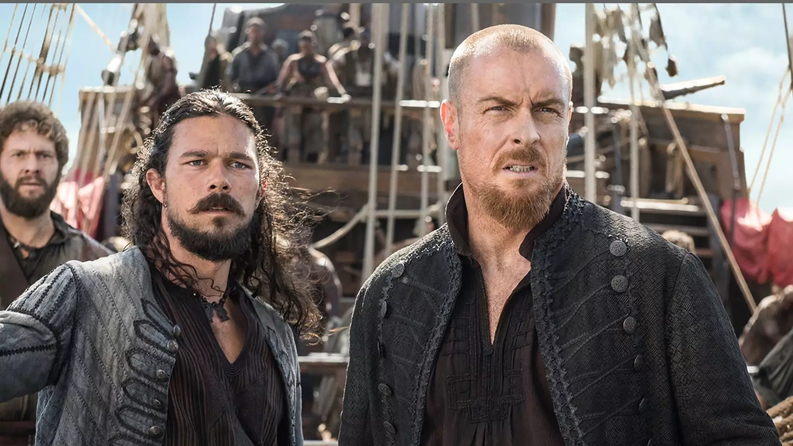 Scene from 'Black Sails' John Silver and Captain Flint on the ship with his crew in the background.