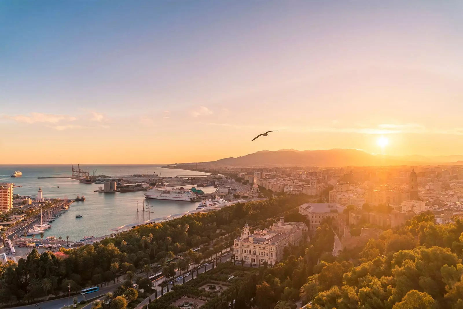 Näkymät Malagaan auringonlaskun aikaan Gibralfarosta, meri vasemmalla ja aurinko laskee vuorten taakse.