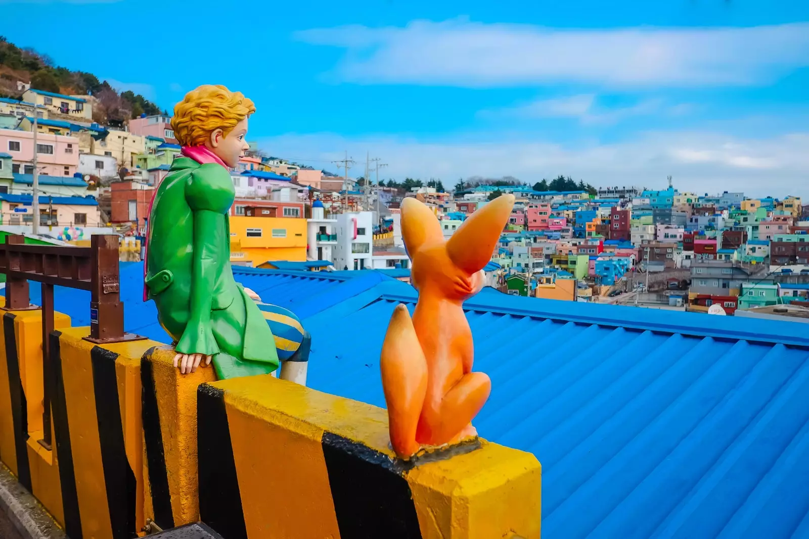 Der kleine Prinz und der Fuchs sitzen auf einem Pavillon mit Blick auf das Meer aus bunten Häusern.