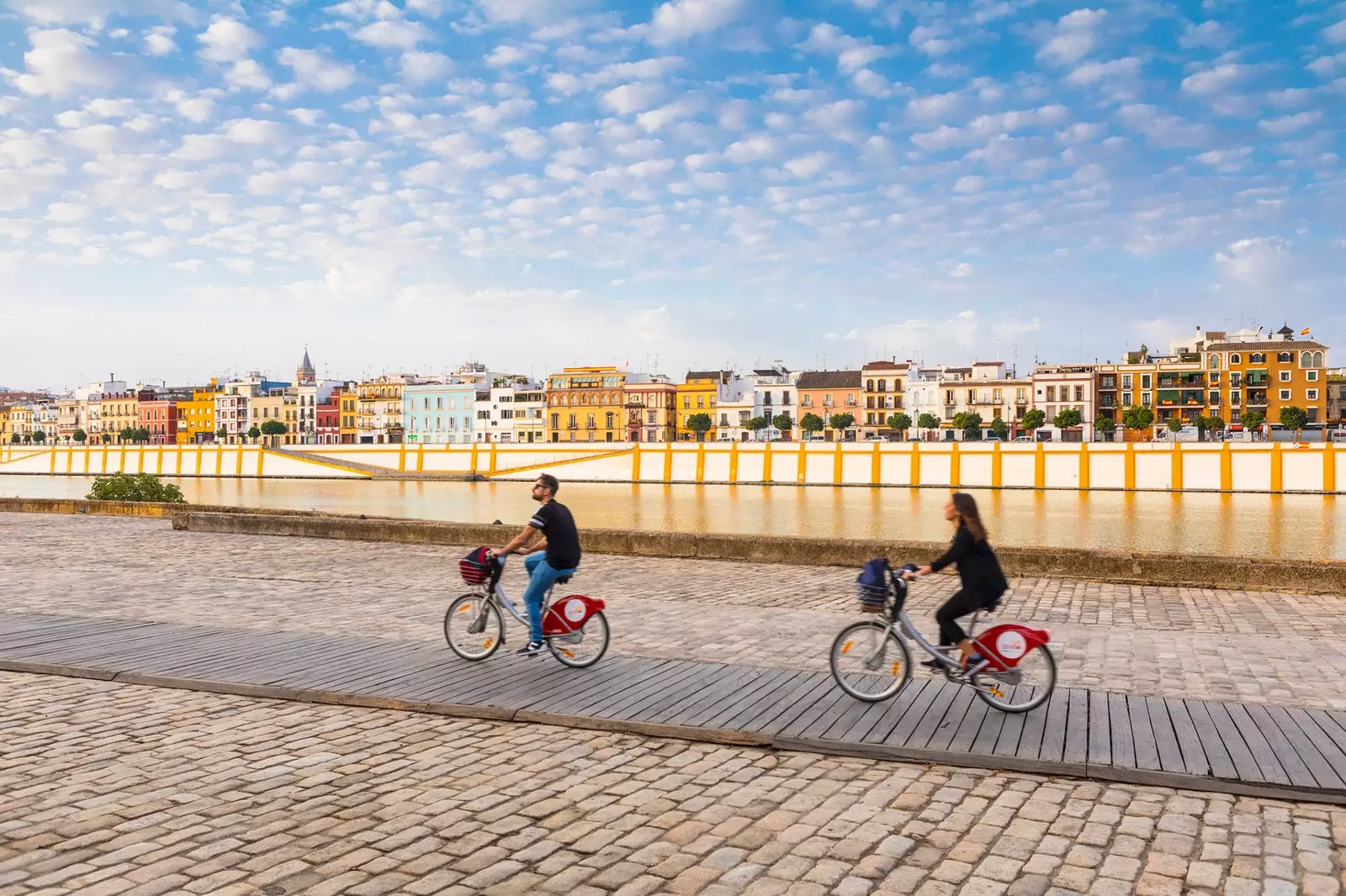 Dvaja ľudia jazdiaci na bicykli pred štvrťou Triana v Seville