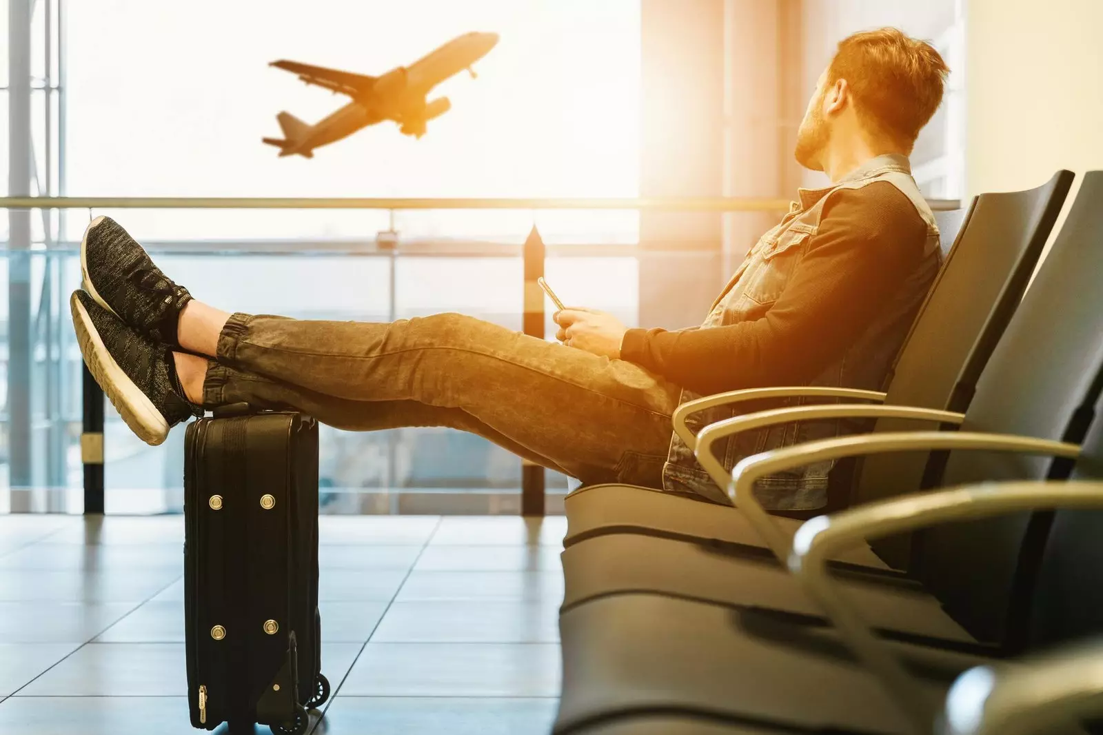 Man sitting in the airport lounge with a carry-on suitcase.