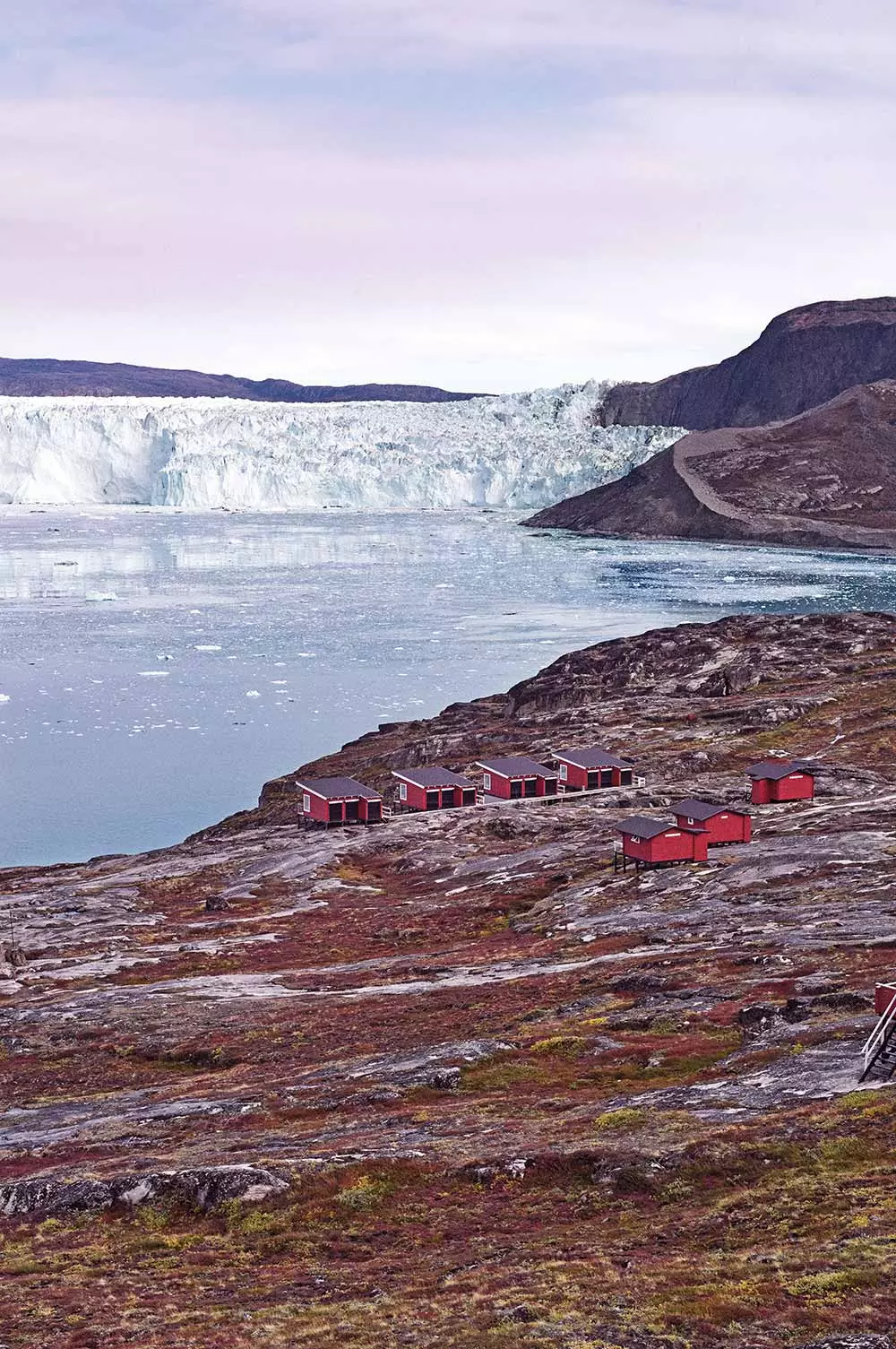 Кабинаҳои сурхи Glacier Lodge Eqi бо пирях дар замина 80 км шимолтар аз Илулиссат ҷойгиранд