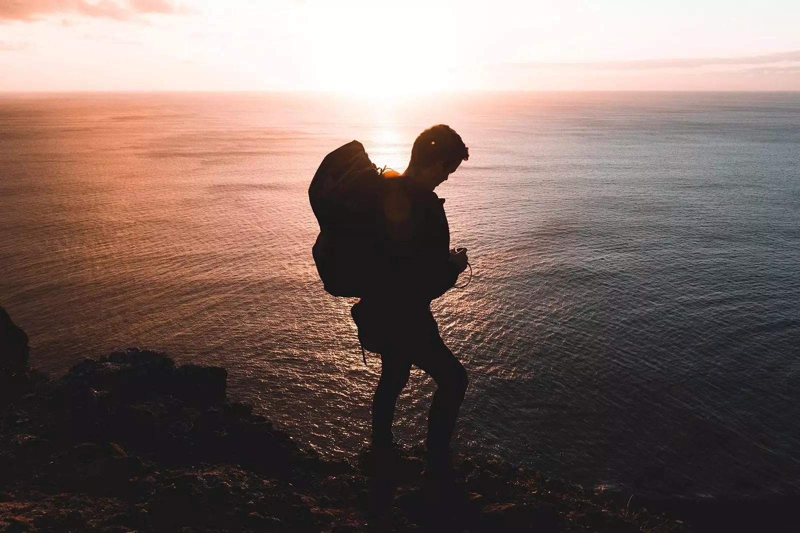 Backpacker-Junge vor dem Meer bei Sonnenuntergang