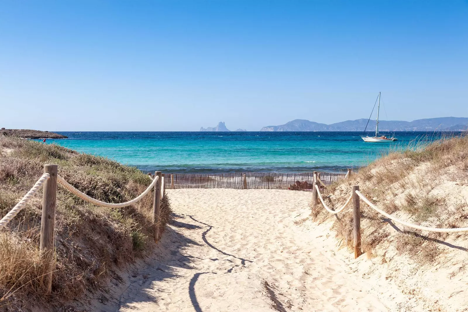 Chemin de sable vers la mer et voilier sur l'eau bleue à Ses Illetes Formentera