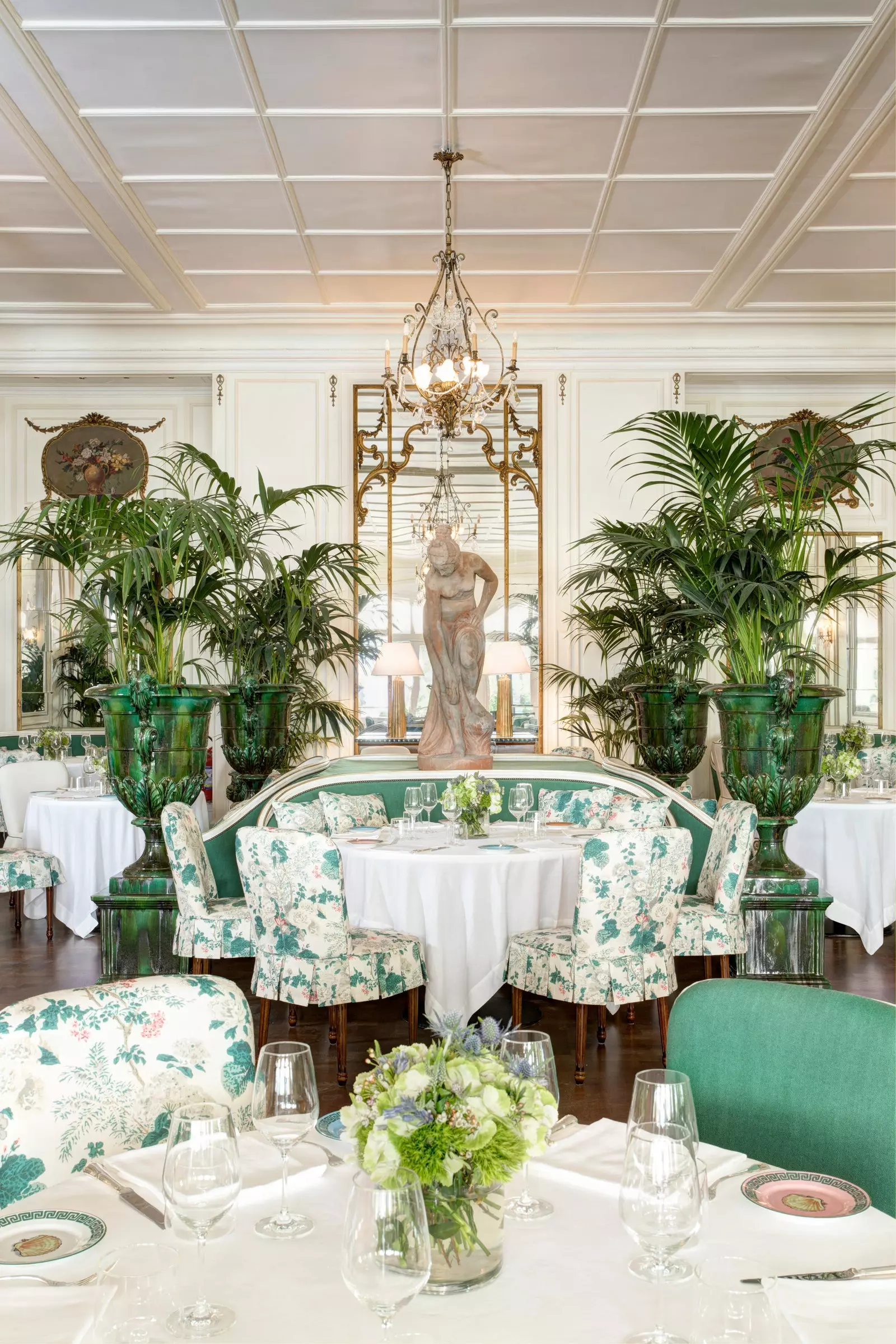 Room decorated in green and white with tables set and a statue in front of a mirror in the background