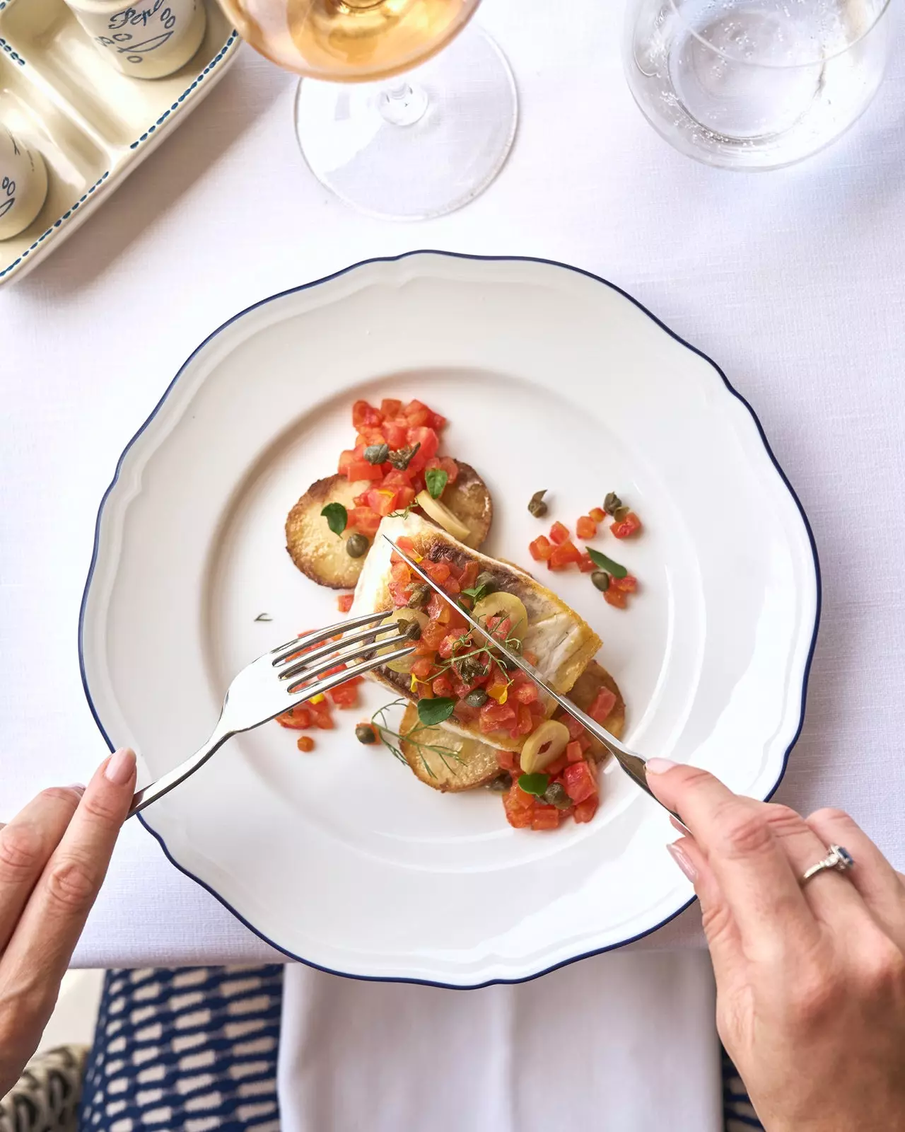 Hands holding knife and fork over a plate of fish and chips