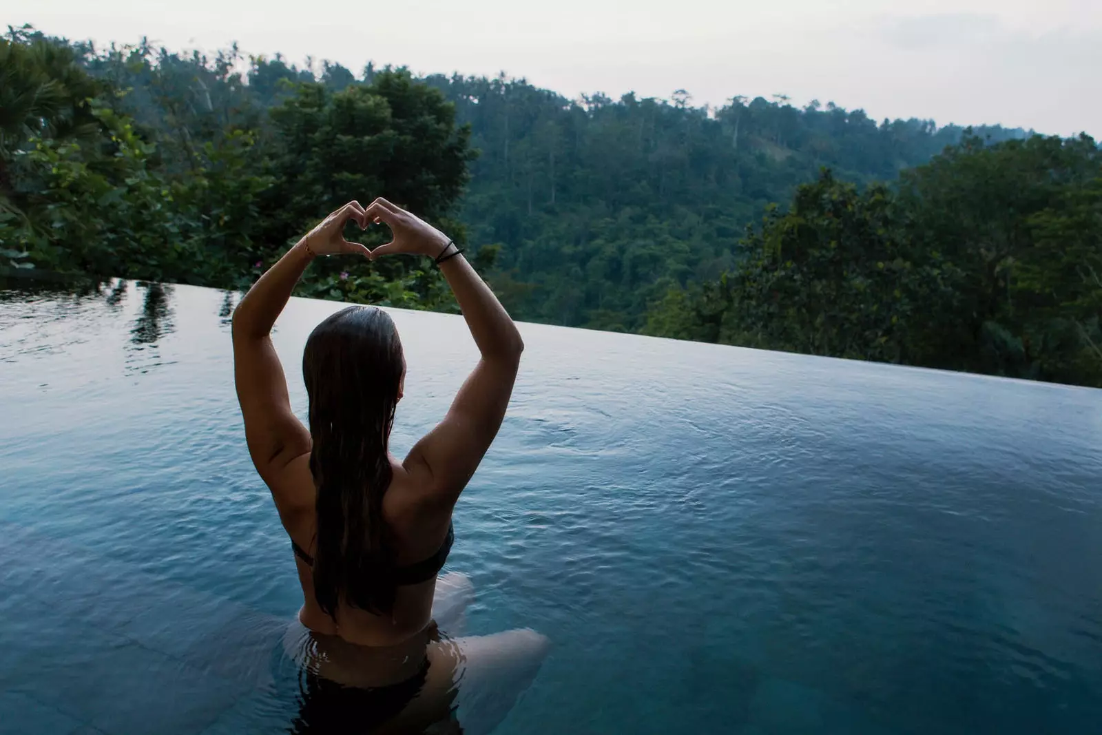 girl making heart with her hands in infinity pool over trees