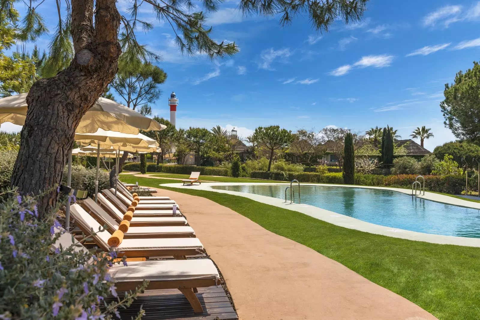 Swimmingpool des Hotels Fuerte El Rompido mit einem der Leuchttürme von El Rompido im Hintergrund.